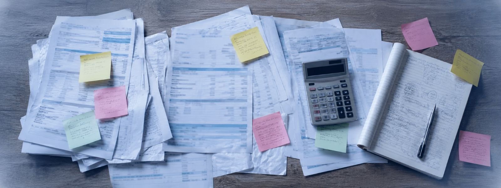 Mesa com extratos impressos, post-its e calculadora, representando controle financeiro manual